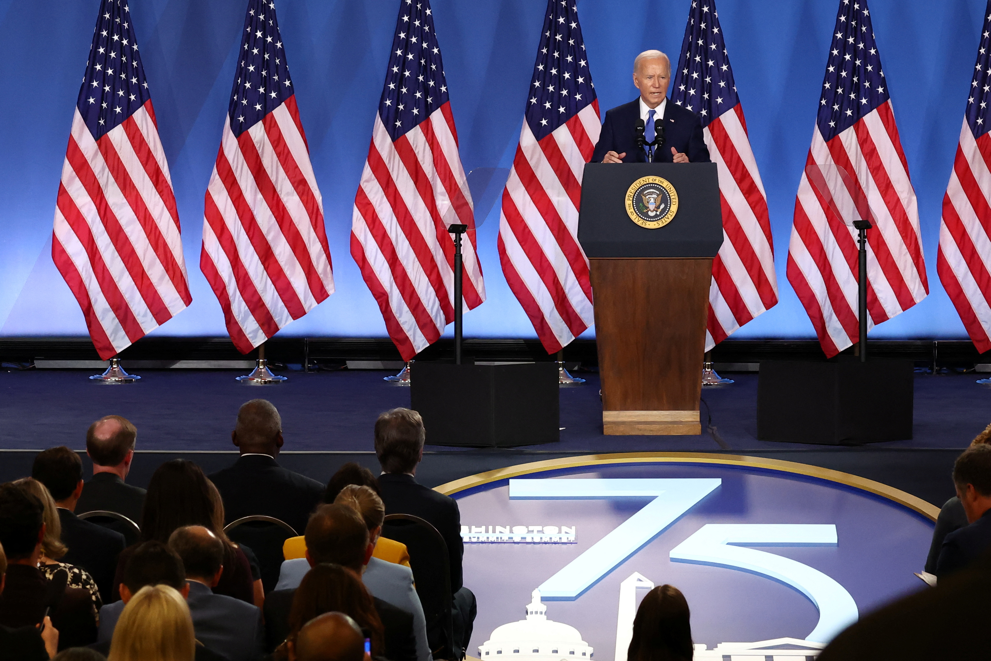 Biden stands in front of a NATO 75 sign at a podium.