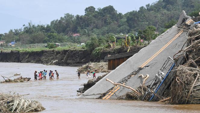 People cross a river near a bridge that collapsed after the river overflowed due to heavy rains brought by tropical storm Trami, in Laurel, Batangas province, south of Manila, October 25 2024. 