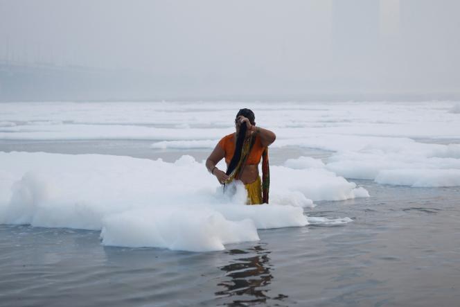 A woman washes her hair in the Yamuna River, polluted by layers of toxic scum, in New Delhi, November 5, 2024.