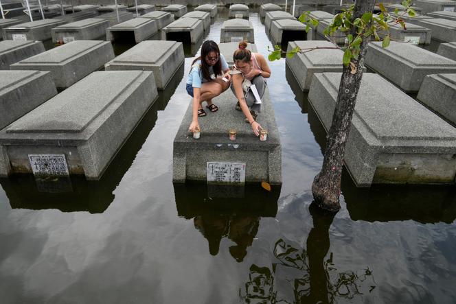 Young women place candles on a half-submerged grave in the Holy Spirit Cemetery in Masantol, Pampanga province, October 31, 2024. 